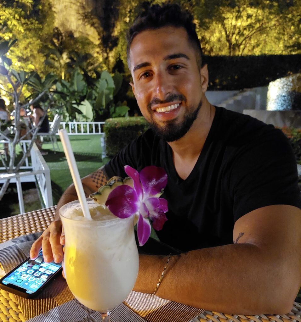 Owity smiling on vacation in Krabi, Thailand, enjoying a tropical cocktail at sunset.
