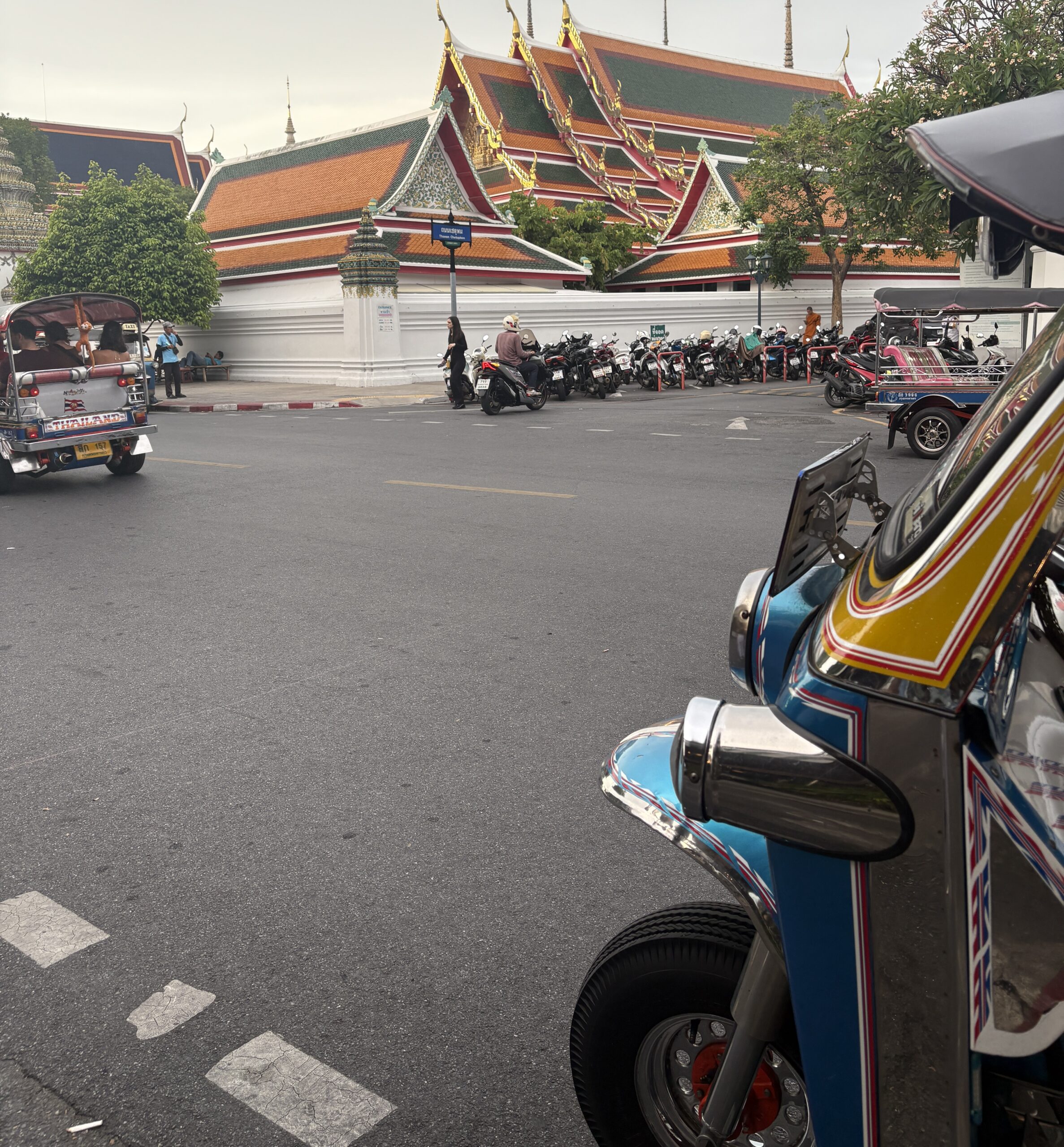 Classic tuk-tuk on a Bangkok street with a traditional Thai temple in the background on a sunny day