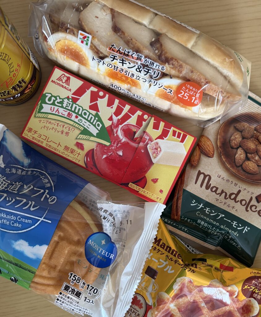 Assortment of snacks and food from 7-Eleven Japan, including egg and chicken sandwich, coffee, nuts, and candy bars