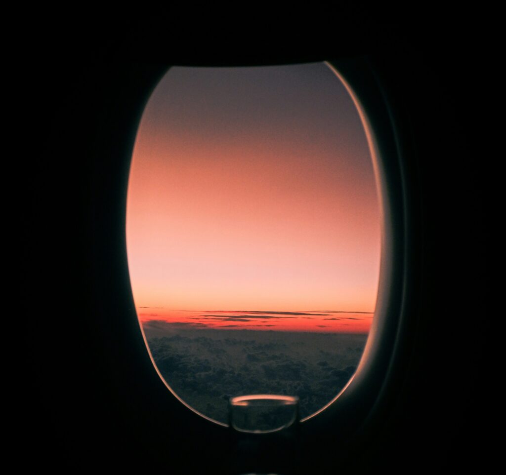 View from airplane window at sunrise with golden sky and clouds below, a perfect travel moment in the air.
