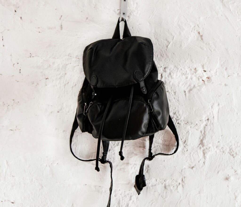 Black backpack hanging on a hook against a white wall background