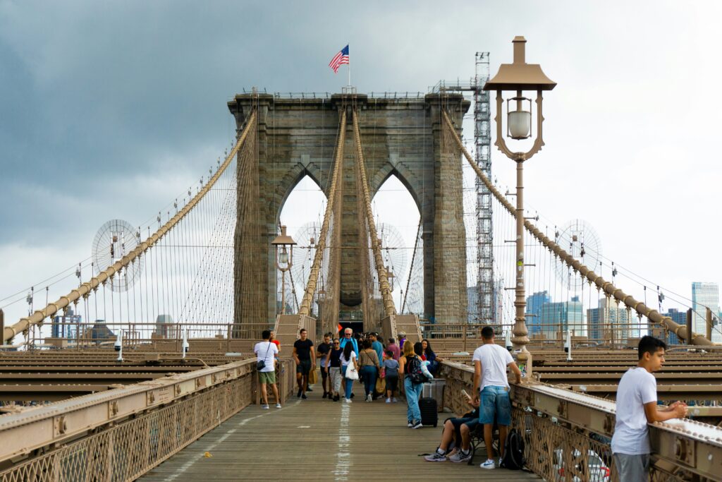 Brooklyn Bridge on a cloudy day with many tourists walking along the pedestrian pathway.