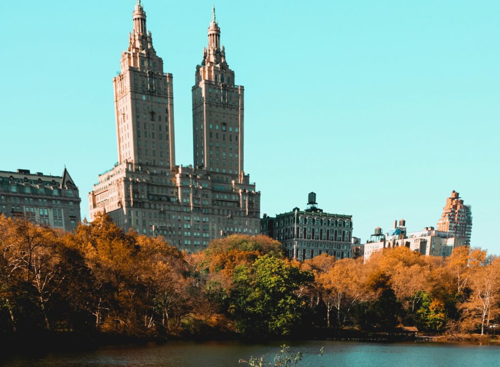Central Park in autumn with vivid fall foliage in the foreground and the twin towers of The El Dorado apartments rising behind the trees.  
