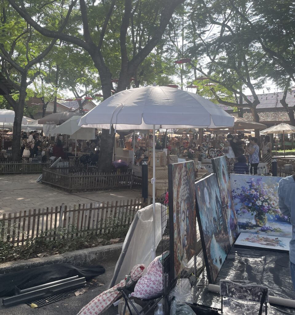 Plenty of locals and tourists browsing stalls at a bustling daytime market in Chiang Mai.