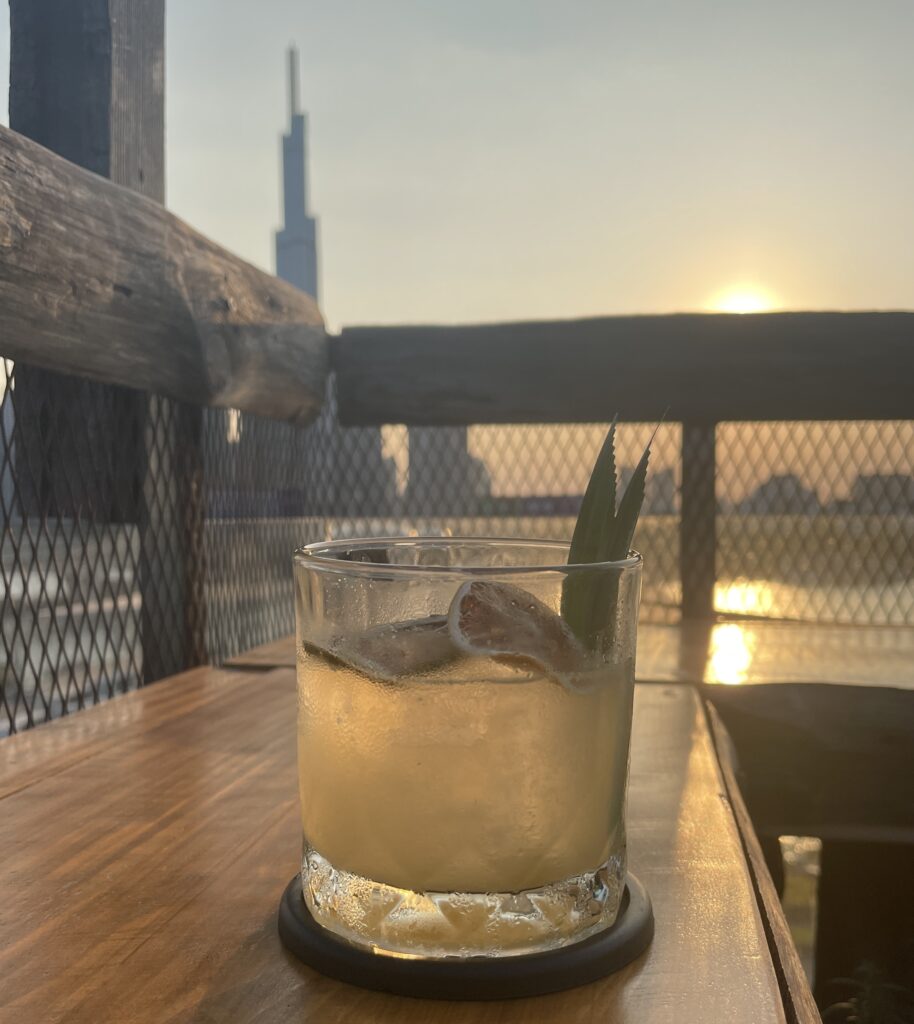 Cocktail at a rooftop bar in Saigon during sunset with Landmark 81 building in the background.