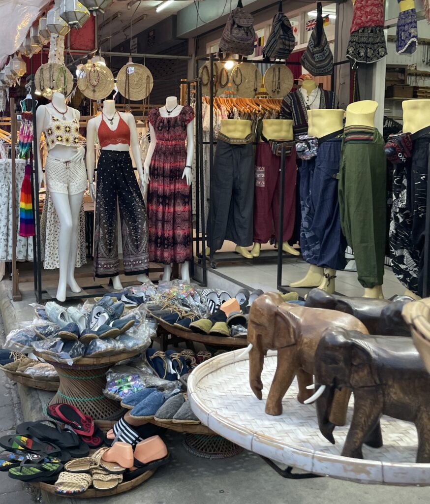 Handcrafted elephant statues with various souvenirs in the background at a Chiang Mai night market, a popular place to shop for unique Thai gifts.
