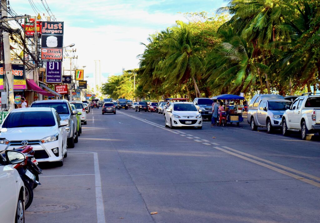 Street view in Jomtien, Thailand with shops, restaurants, and cars near the beach
