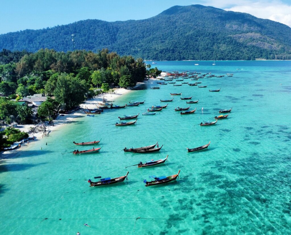 Aerial view of longtail boats in Koh Lipe surrounded by turquoise and deep blue water, showcasing lush natural beauty.
