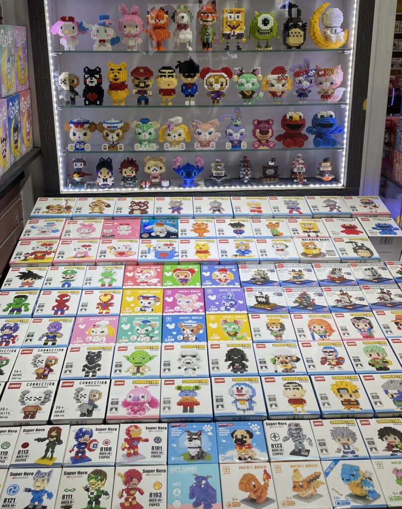 Colorful LEGO-style figurines of popular characters from games and shows displayed at a market stall in Thailand.
