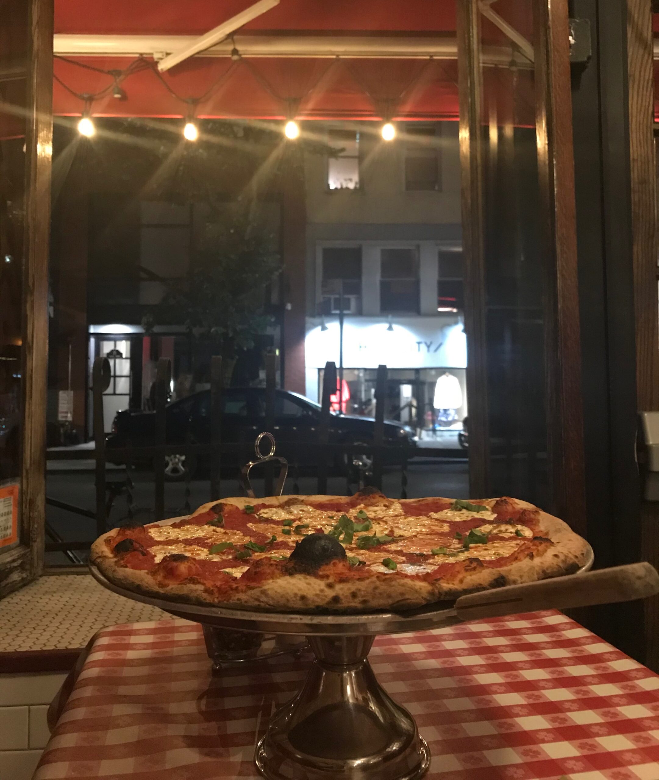Lombardi’s pizza served in Little Italy, New York City, with a street view of the neighborhood.