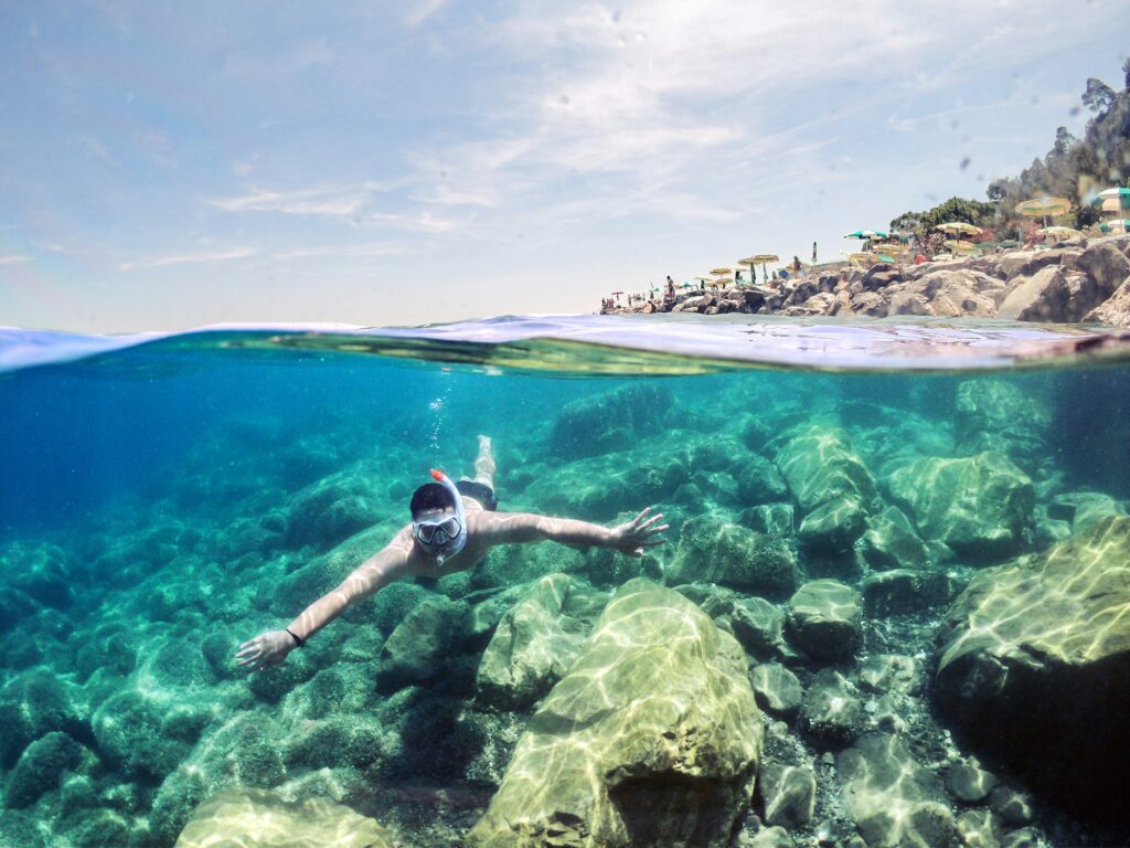 Man snorkeling in clear tropical water with both above and below surface visible