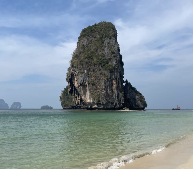 Early morning view of Phra Nang Cave Beach in Railay, Thailand, featuring a dramatic limestone cliff rising from the turquoise water.