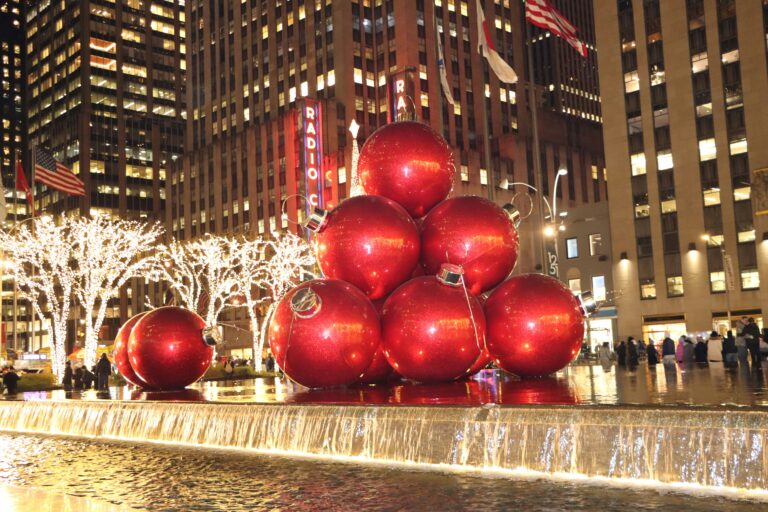 Massive red Christmas ornaments at Radio City in New York City with bright lights and tourists.