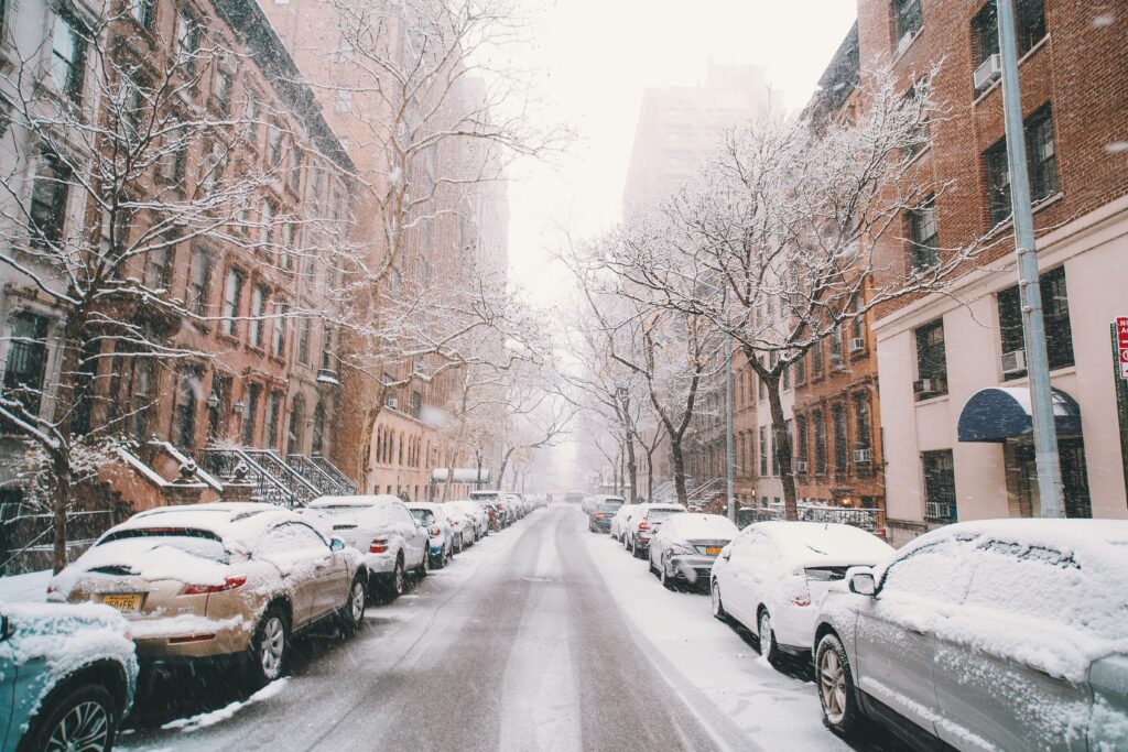 Snow-covered street in New York City on a February afternoon with parked cars and sidewalks blanketed in fresh snow.