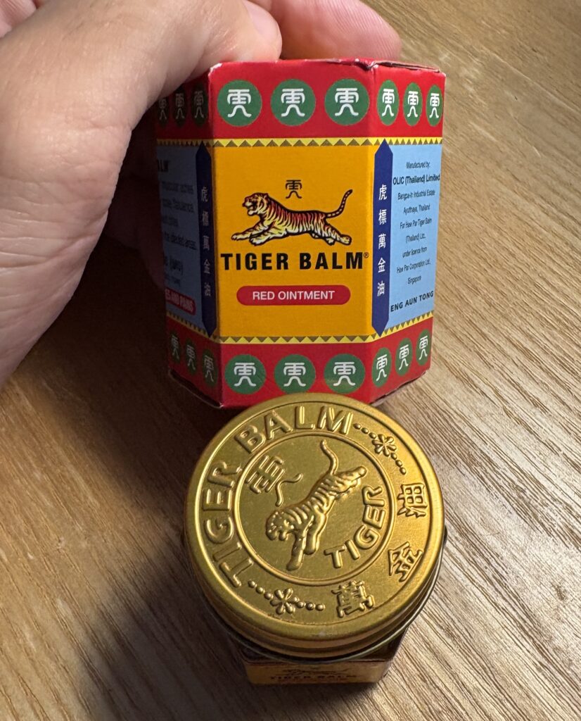 Close-up of a Tiger Balm red jar purchased in Thailand, a popular herbal remedy used for pain relief and colds.
