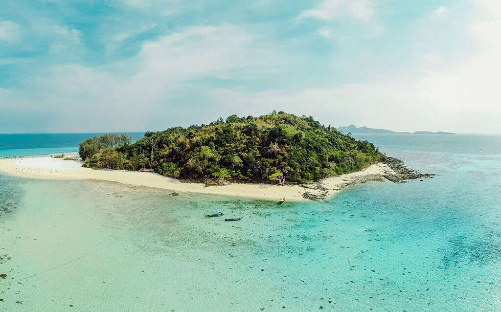 Aerial view of Bamboo Island in the Phi Phi Islands, showing turquoise waters, soft white sand, and lush greenery surrounded by the Andaman Sea.
