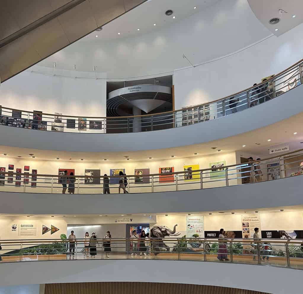 Interior of the Bangkok Art and Culture Centre showing multiple floors of cultural art exhibits and people walking.