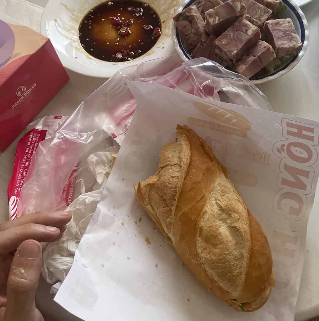 A banh mi sandwich from Banh Mi Hong Hoa on a table, served with Vietnamese cold cuts, intestines, and a soy-chili dipping sauce.