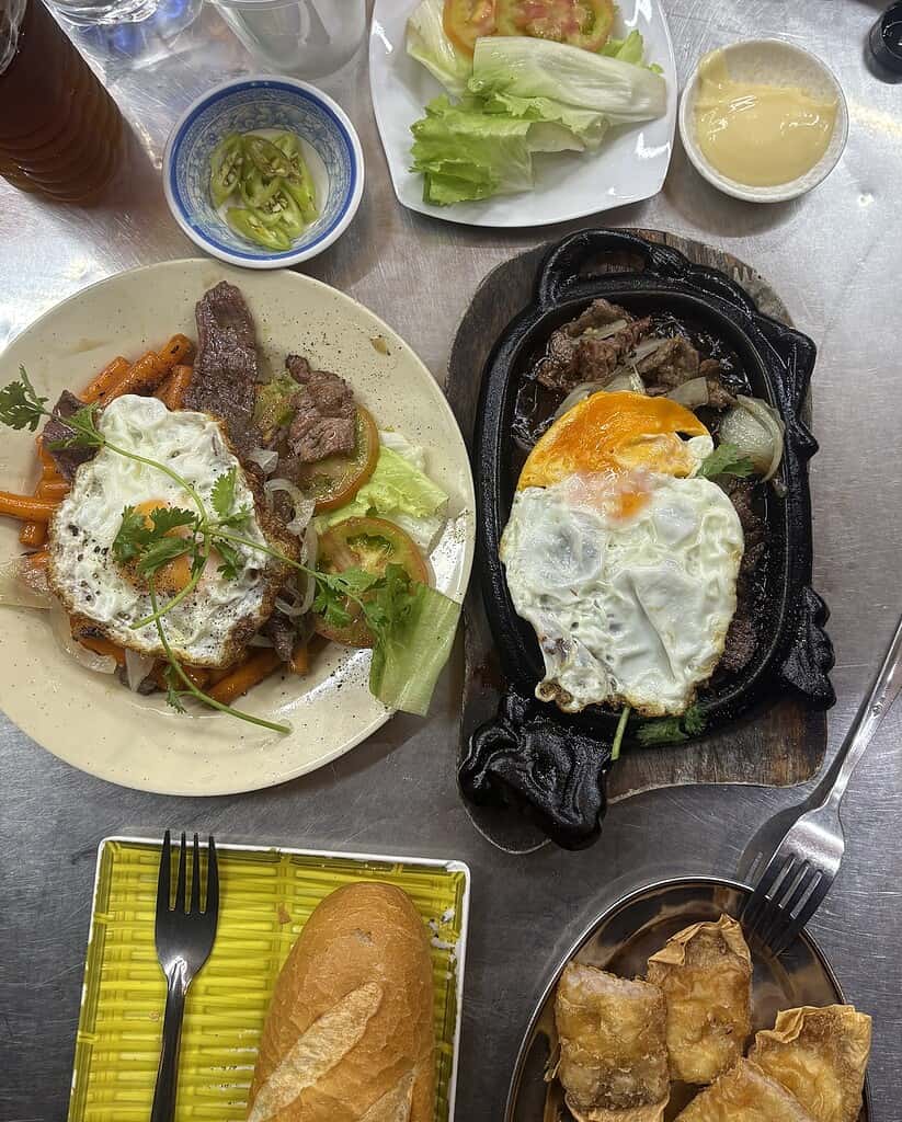 Bo Ne and Bo Nui dishes with drinks on a metal table in Saigon, served during a late evening meal.
