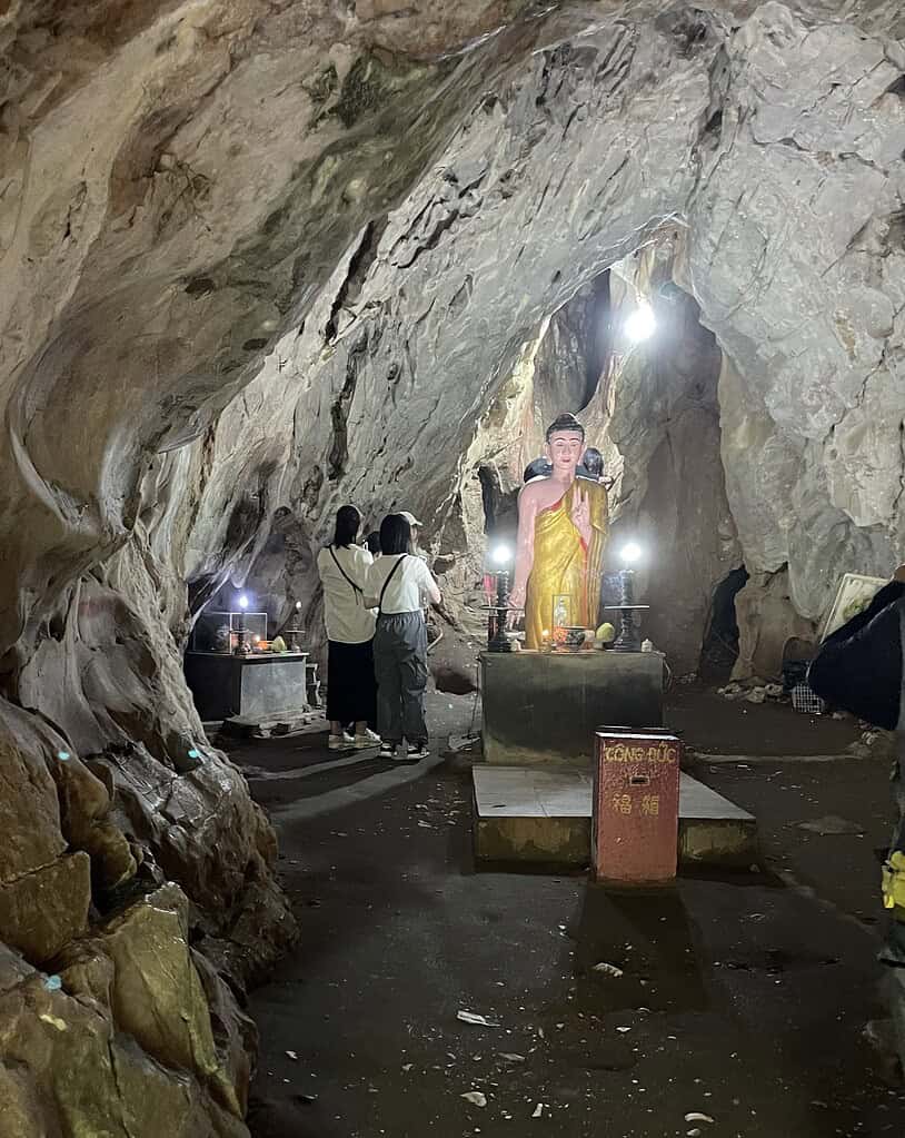 A Buddha temple set deep within a cave at the Marble Mountains in Da Nang, with two local Vietnamese women respectfully paying homage.