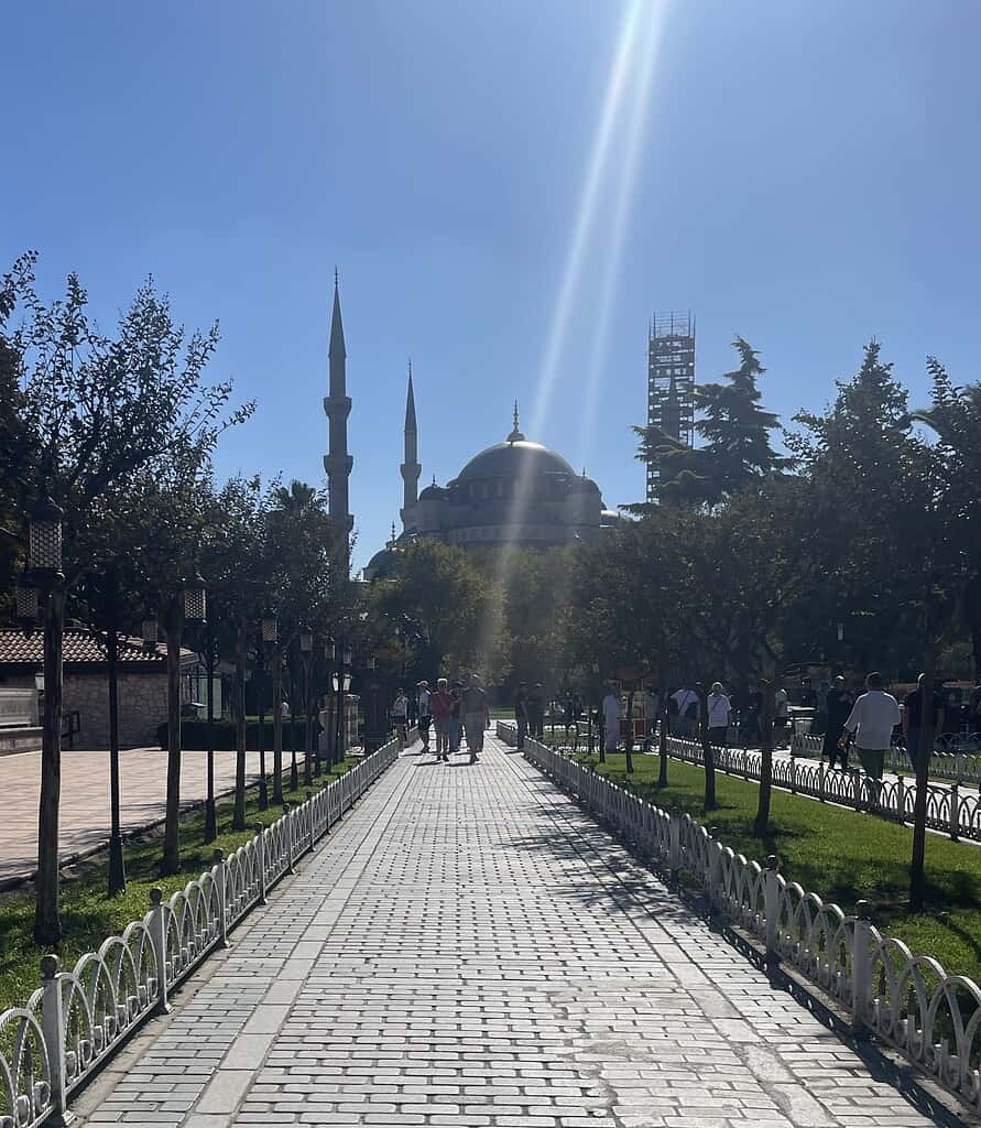 Sunny day scene with locals and tourists walking along a cobblestone pathway toward the Hagia Sophia mosque in Istanbul.