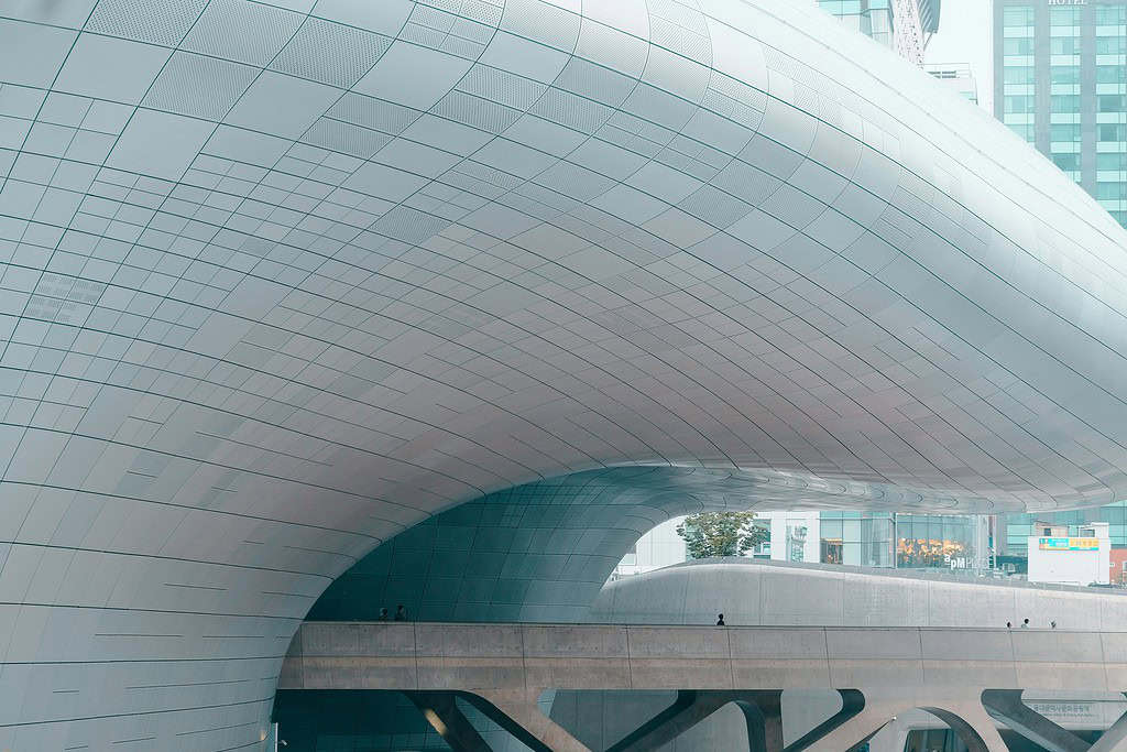 Unique angle of Dongdaemun Design Plaza in Seoul showing its modern architecture, with a few tourists walking across the bridge.