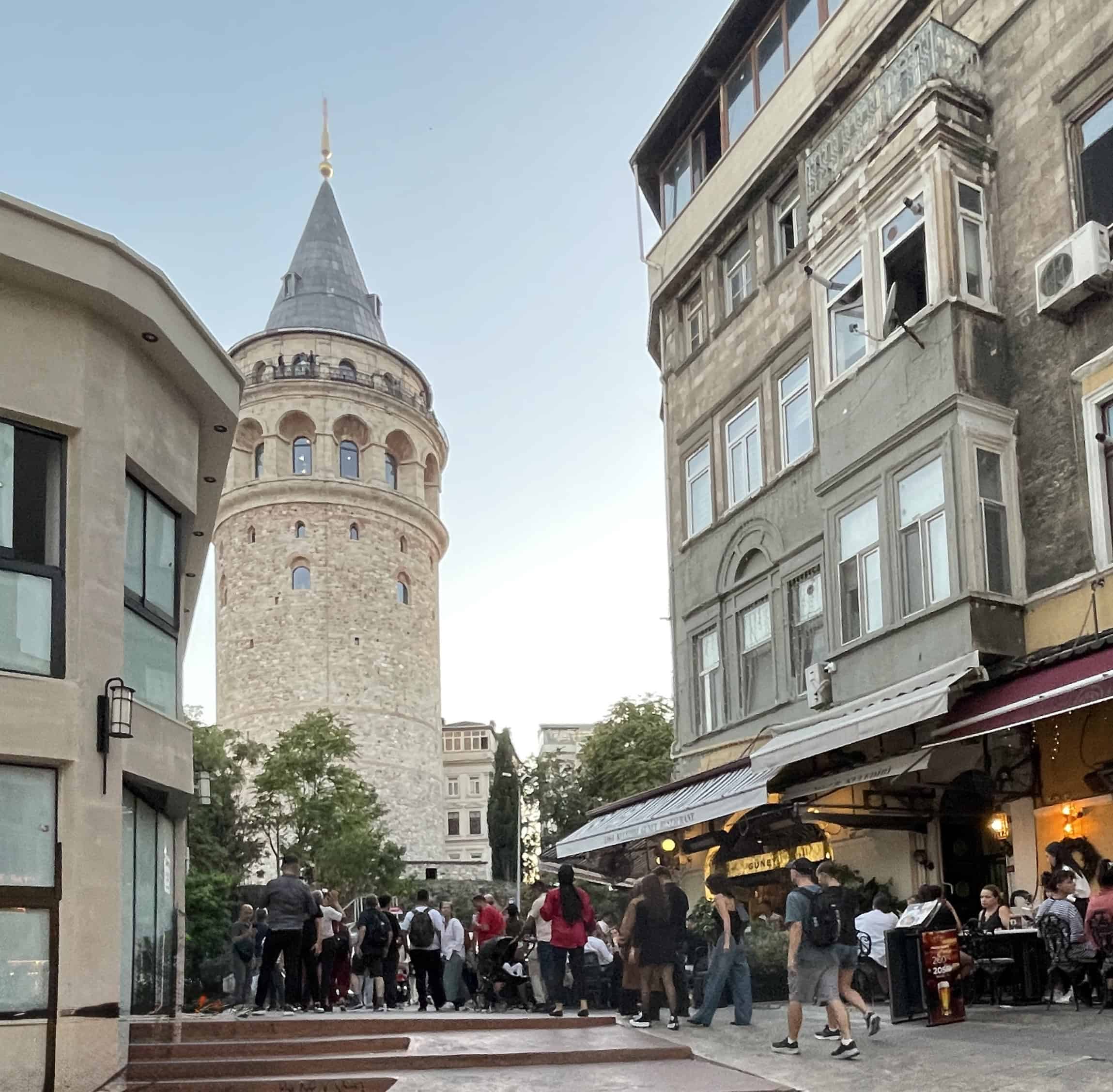 Galata Tower in Istanbul during the evening with many locals walking nearby, surrounded by cafés and a lively street scene.