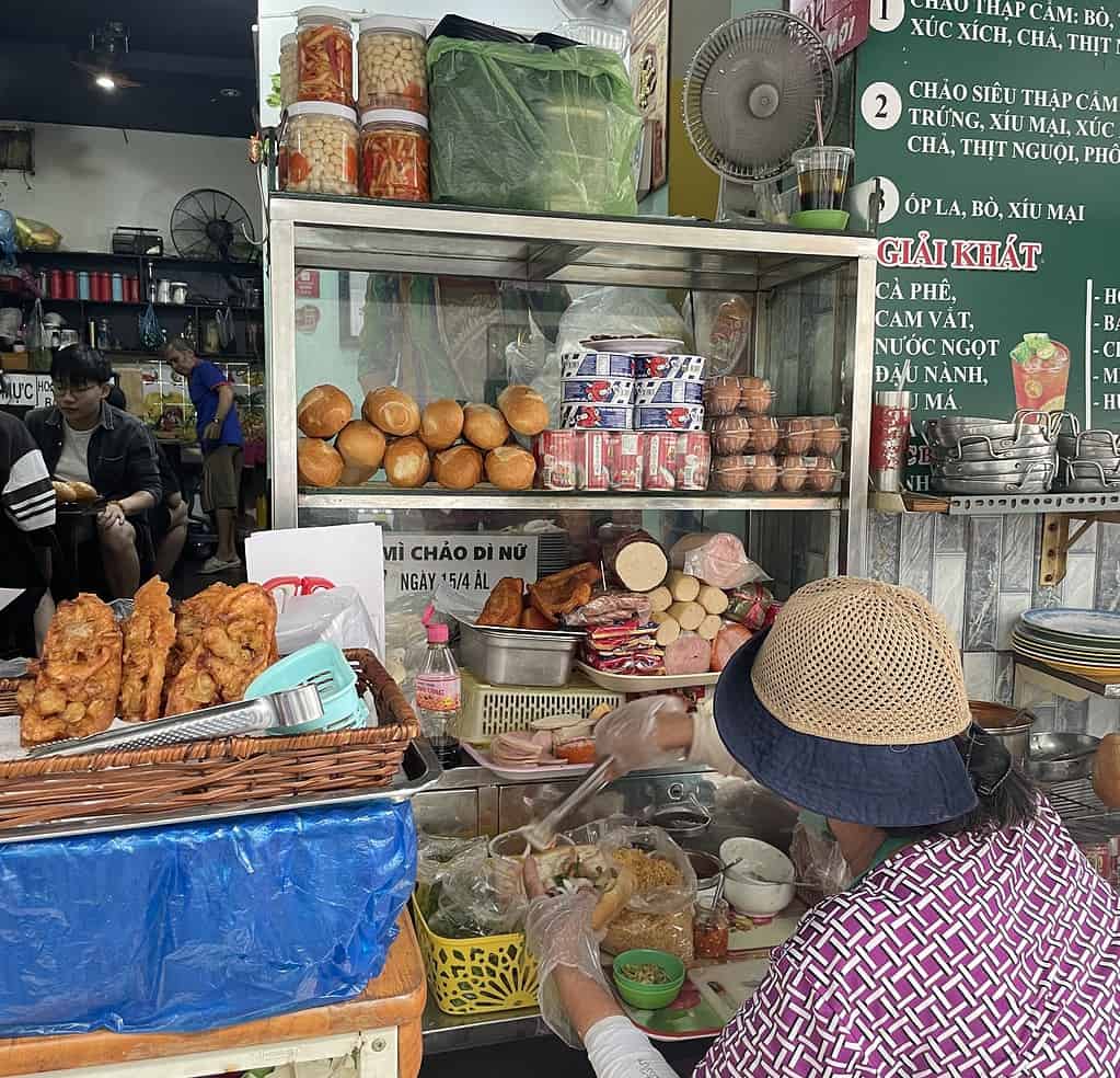Grandma preparing Vietnamese breakfast dishes in a Saigon alleyway kitchen, part of a local Bo Ne and banh mi restaurant.