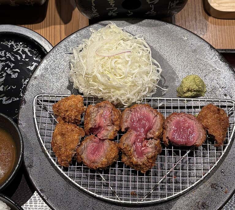 Close-up of Gyukatsu with bright pink beef cutlet, shredded cabbage salad, a side of wasabi, miso soup, and Japanese curry.