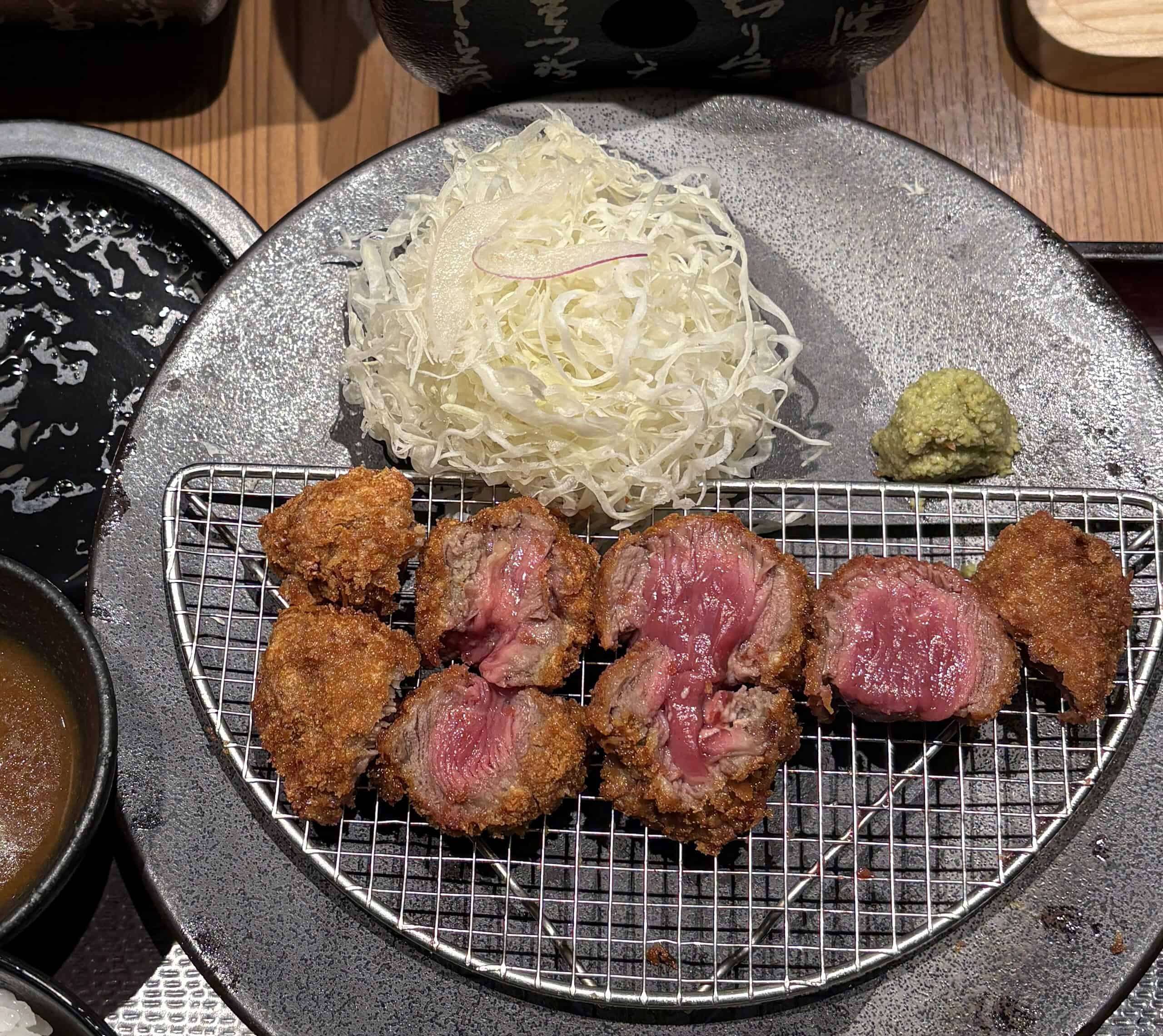 Close-up of Gyukatsu with bright pink beef cutlet, shredded cabbage salad, a side of wasabi, miso soup, and Japanese curry.