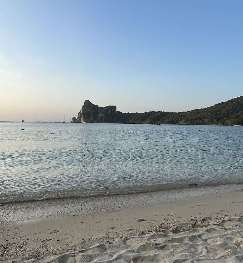 Peaceful evening view of Loh Dalum Bay with calm waters and limestone cliffs in the distance on Phi Phi Island.
