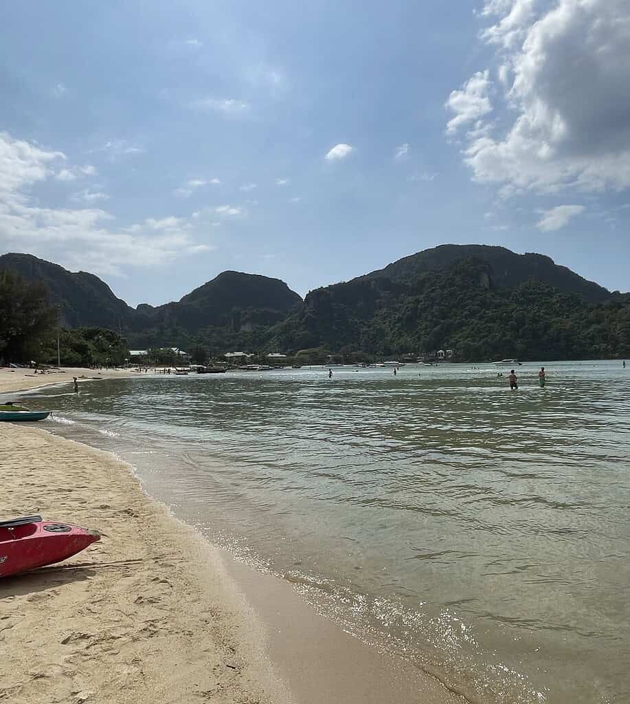 Tourist in the clear waters of Loh Dalum Bay with a kayak resting on the beach and limestone cliffs in the background on Phi Phi Island.
