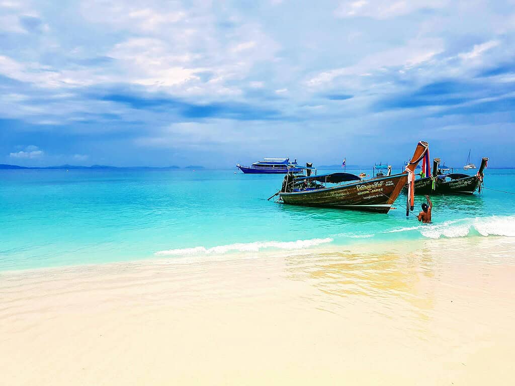 Man standing by his traditional longtail boat in the crystal-clear waters of Long Beach, Phi Phi Island.