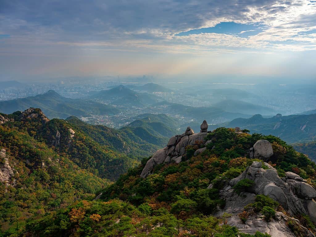 Breathtaking view from the top of Munsu Peak in Bukhansan, South Korea, with rugged rocks, lush greenery, and a distant glimpse of the city — a peaceful escape that feels far removed from Seoul.