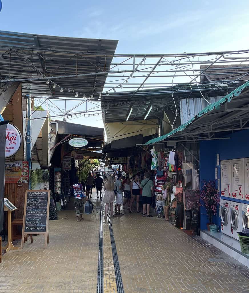 Walkway in Phi Phi Island with laundry machines on the right and restaurants and a Thai massage spot on the left.