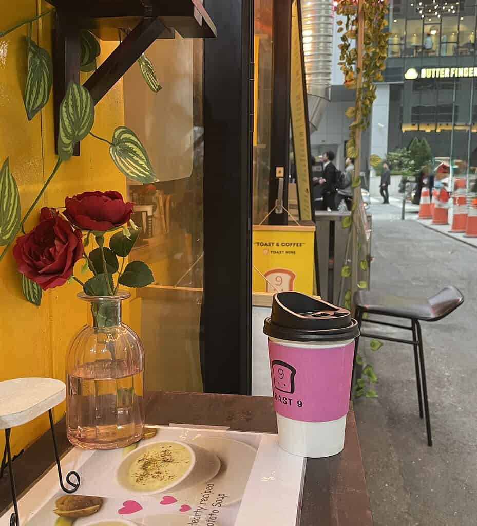 Charming alleyway café in Seoul with a small table set for one, featuring a latte and roses, looking out toward the main road ahead, a peaceful coffee moment tucked away from the bustle.