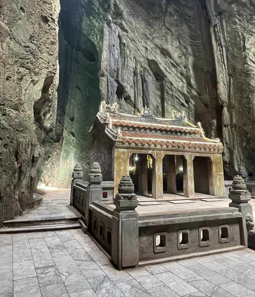 A temple-like structure illuminated by natural light inside a cave at the Marble Mountains in Da Nang, creating a dramatic and unique atmosphere.