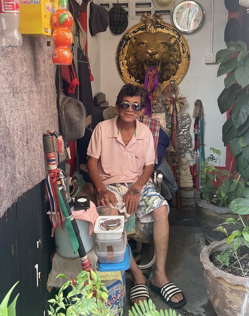 Thai man smiling at his home in Chiang Mai, surrounded by plants and home decor elements.
