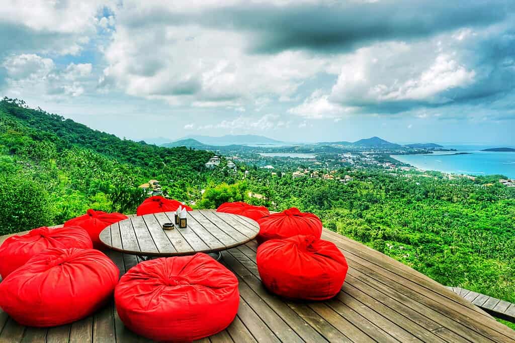 Large red couches at The Cocoon Samui Viewpoint overlooking a scenic mountain and coastline panorama.
