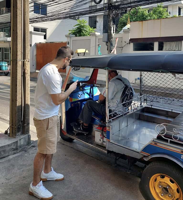 The creator of Travel Hiatus settling change with a tuk tuk driver on a sunny day in Bangkok, Thailand.