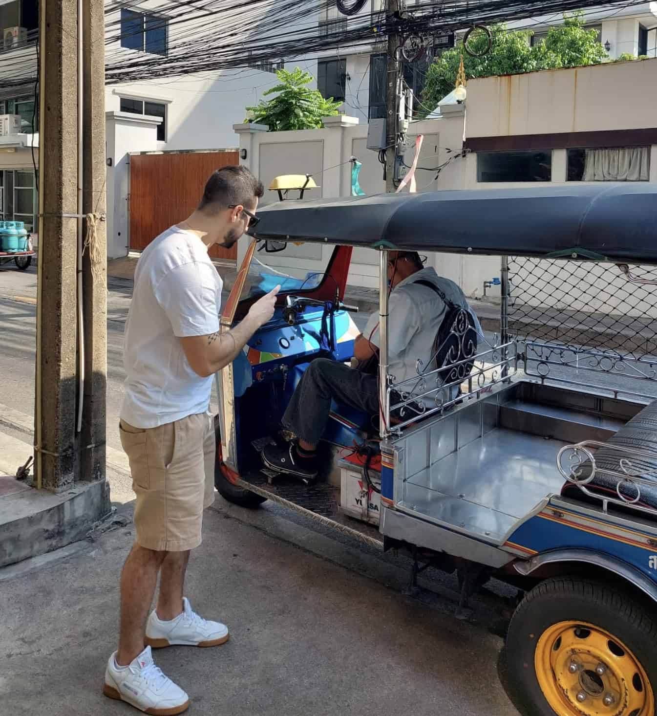 The creator of Travel Hiatus settling change with a tuk tuk driver on a sunny day in Bangkok, Thailand.