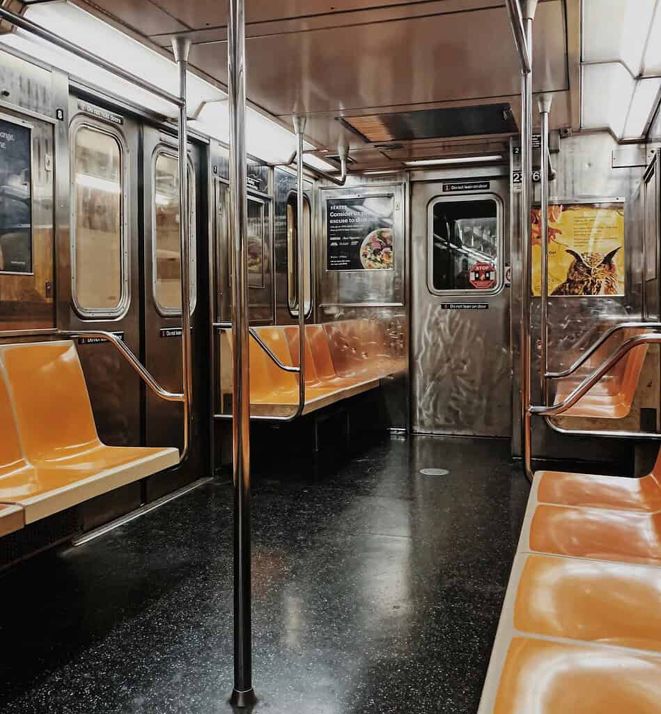 Interior of an empty New York City subway car with silver poles and orange seats during off-peak hours
