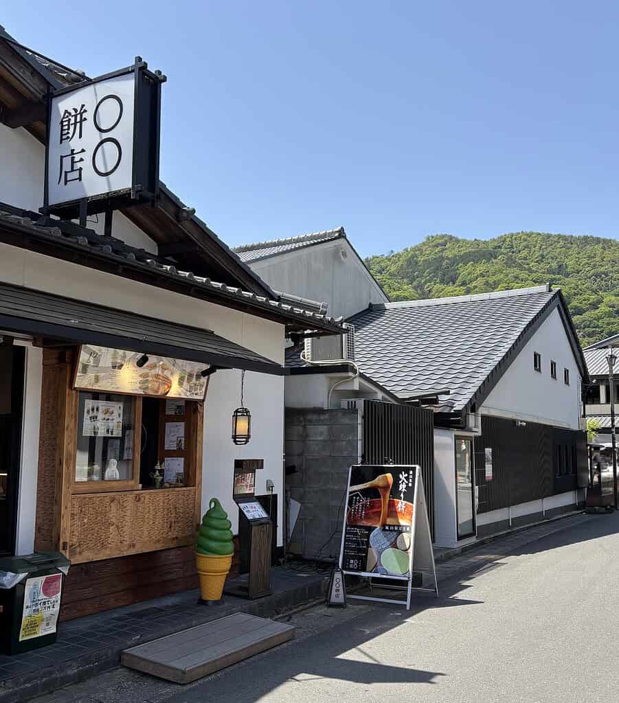Small shop selling matcha desserts and drinks on a quiet side street in Arashiyama, with green mountain scenery in the background
